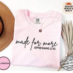 Puede incluir: Camiseta rosa con el texto "made for more" y "EPHESIANS 2:10" en letras negras.