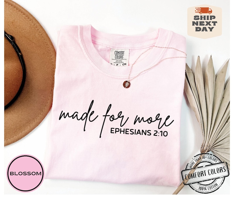 Puede incluir: Camiseta rosa con el texto "made for more" y "EPHESIANS 2:10" en letras negras.