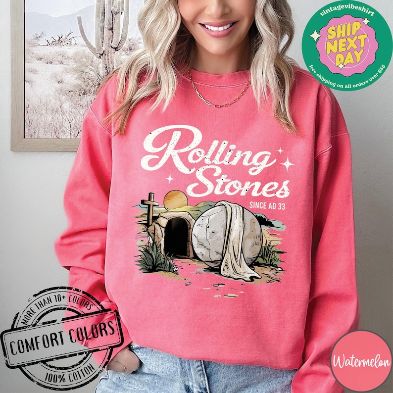 May include: A pink sweatshirt with a distressed white graphic that says "Rolling Stones Since AD 33". The graphic features a stone tomb with a cross and a white cloth draped over it.