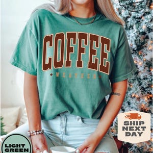 May include: A light green t-shirt with the text "COFFEE WEATHER" in brown and gold lettering. The shirt is being worn by a person.