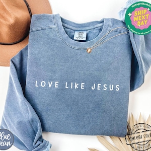 May include: A blue sweatshirt with the text "LOVE LIKE JESUS" in white lettering. The sweatshirt is made of a soft, comfortable fabric and has a relaxed fit.