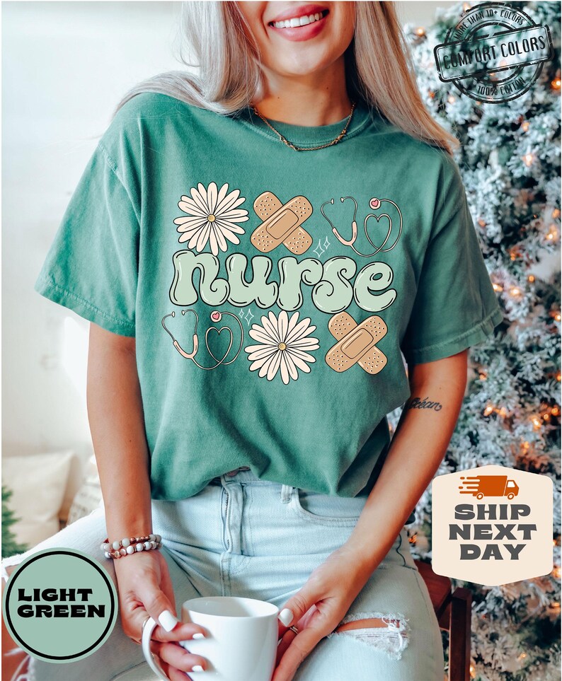 May include: A light green t-shirt with the word "nurse" in a retro font. The shirt is decorated with white daisies, red hearts, and plasters.