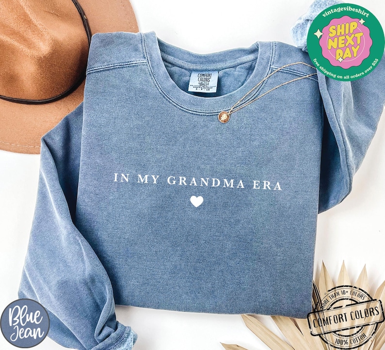 May include: A blue sweatshirt with the text "IN MY GRANDMA ERA" and a small white heart in the center.