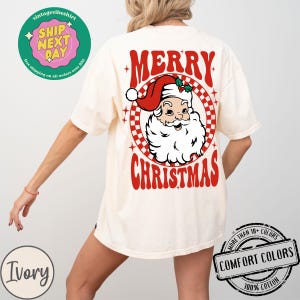 May include: Ivory t-shirt with a red and white retro design featuring Santa Claus and the text "Merry Christmas".