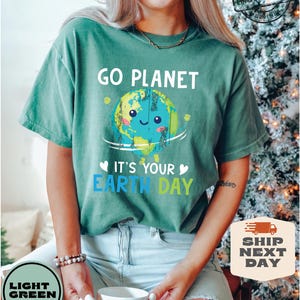May include: A light green t-shirt with the text "Go Planet" and a cartoon image of the Earth with a smiling face. The text "It's Your Earth Day" is below the image.