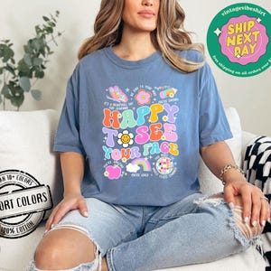 May include: A blue t-shirt with a colorful graphic that says "Happy to see your face". The graphic features a rainbow, a smiley face, a flower, and a butterfly. The shirt is made of 100% cotton and is available in a variety of colors.
