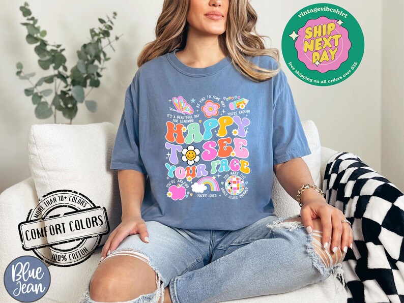 May include: A blue t-shirt with a colorful graphic that says "Happy to see your face". The graphic features a rainbow, a smiley face, a flower, and a butterfly. The shirt is made of 100% cotton and is available in a variety of colors.
