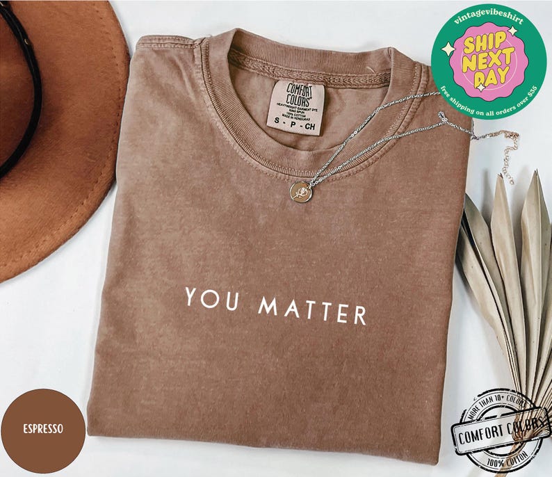May include: A brown t-shirt with the text "YOU MATTER" printed in white on the front. The shirt is made of 100% cotton and is available in a variety of sizes.