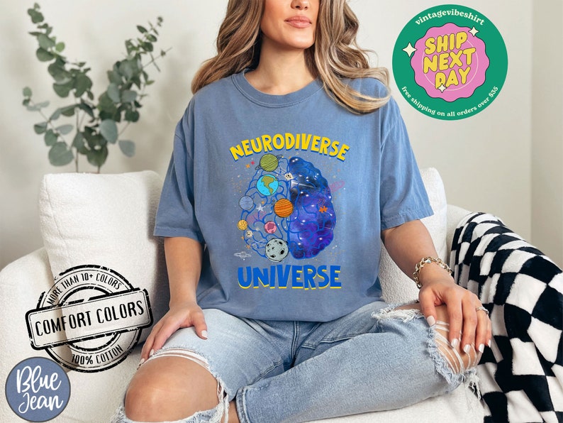 Op de afbeelding: Een blauw t-shirt met een afbeelding van een brein met planeten en sterren erin. De tekst "Neurodiverse Universe" staat op het t-shirt gedrukt.