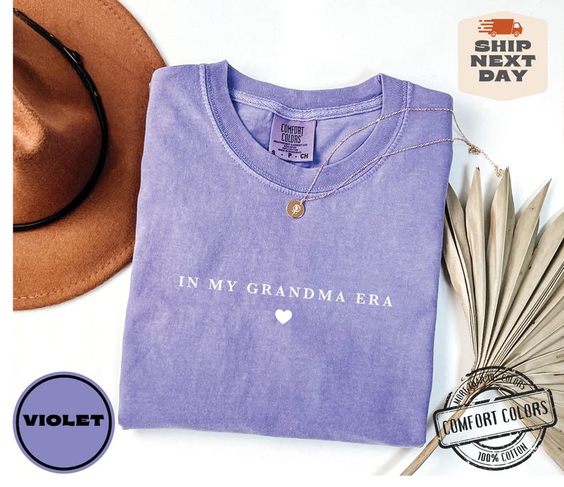May include: Purple t-shirt with the text "In My Grandma Era" and a white heart. The shirt is made of 100% cotton.