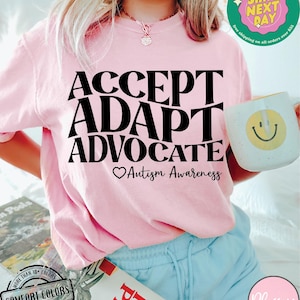 May include: Pink t-shirt with the text "ACCEPT ADAPT ADVOCATE" in black lettering. Below the text is a heart symbol and the words "Autism Awareness".