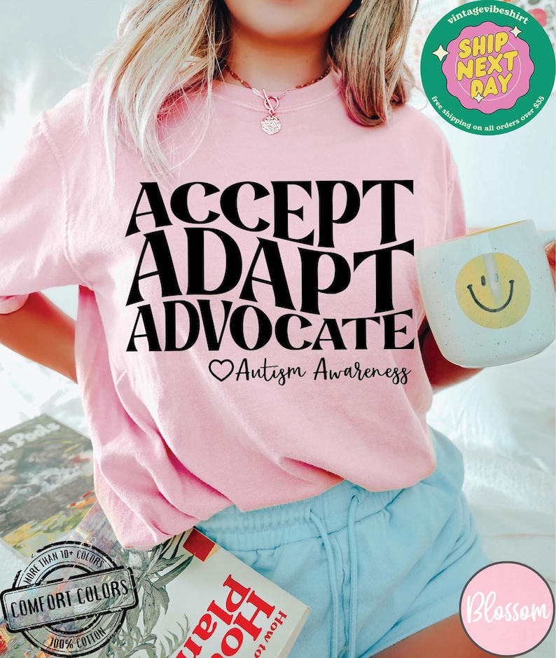 May include: Pink t-shirt with the text "ACCEPT ADAPT ADVOCATE" in black lettering. Below the text is a heart symbol and the words "Autism Awareness".