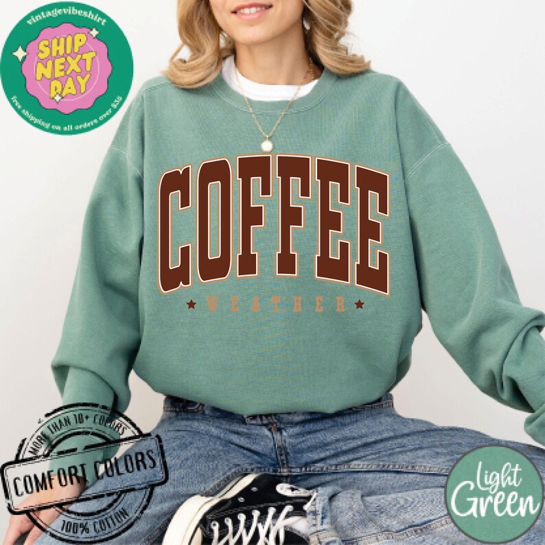 May include: A light green sweatshirt with the text "COFFEE WEATHER" in brown letters. The sweatshirt is made of 100% cotton and is available in a variety of colors.