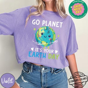 May include: Purple t-shirt with a cartoon image of the Earth smiling and holding a sign that says "Go Planet It's Your Earth Day".