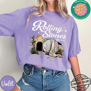 May include: Purple t-shirt with a graphic of a stone rolling away from a tomb with the text "Rolling Stones Since AD 33".