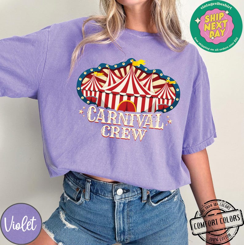 May include: Violet Comfort Colors t-shirt with a carnival tent graphic. The graphic features red and white striped tents with the words "CARNIVAL CREW". The shirt is made of 100% cotton.