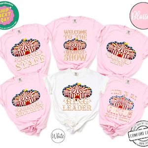 May include: Pink and white t-shirts with circus-themed designs. The shirts feature a circus tent graphic with text such as "Carnival Staff," "Greatest Show," and "Ring Leader." The shirts are made of 100% cotton.