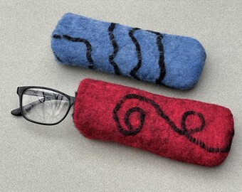 May include: Two rectangular felted cases for eyewear. One case is blue with black wavy lines, and the other is red with a black swirling pattern. A pair of black-framed spectacles is partially inserted into the red felted case, showing the lenses.