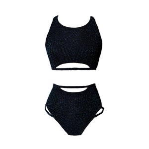 May include: A black two-piece outfit with a sparkly texture. The top is a halter style with a cutout in the front. The bottoms are high-waisted and have a cut-out detail on the sides.