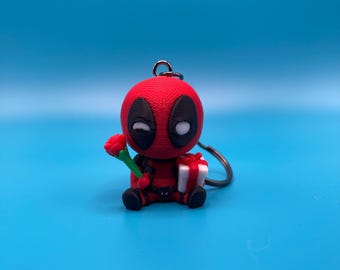 May include: A red and black Deadpool character keychain holding a red rose and a white gift box.