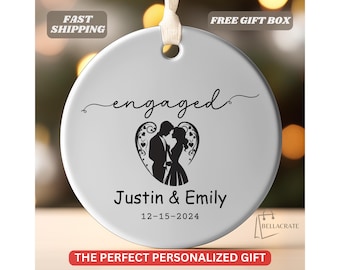 May include: White round ornament with a black silhouette of a couple embracing inside a heart with the text "engaged" above and "Justin & Emily 12-15-2024" below.