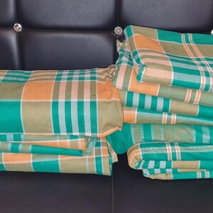 Puede incluir: Una pila de tela a cuadros verde y naranja doblada. La tela est&aacute; doblada en forma rectangular y est&aacute; sentada en un sof&aacute; de cuero negro.