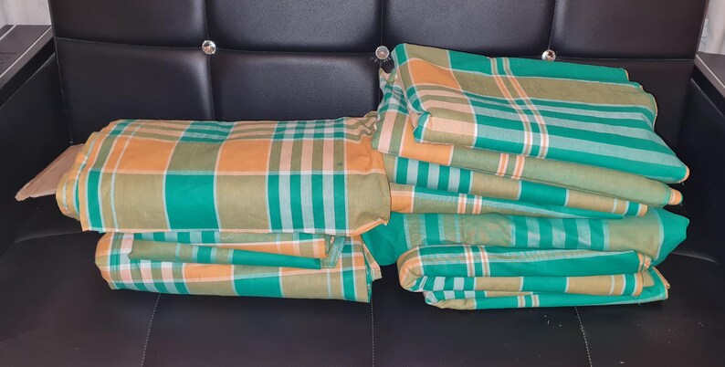 Puede incluir: Una pila de tela a cuadros verde y naranja doblada. La tela est&aacute; doblada en forma rectangular y est&aacute; sentada en un sof&aacute; de cuero negro.