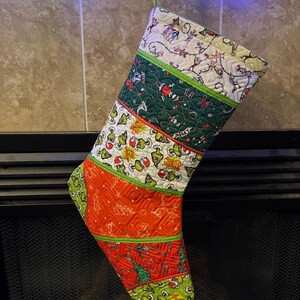 May include: A Christmas stocking with a green, red, and white patchwork design featuring a Grinch theme. The stocking is hanging from a fireplace mantel.