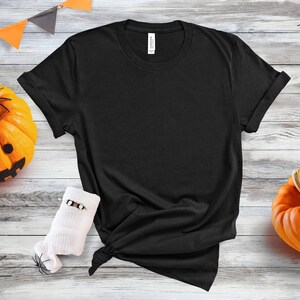May include: A black t-shirt with rolled up sleeves, lying on a white wooden surface with two orange pumpkins and black spiders.