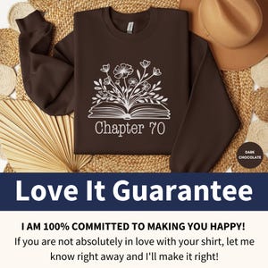May include: A brown sweatshirt with a white design of a book with flowers growing out of it. The text "Chapter 70" is printed below the book. The sweatshirt is on a woven straw background.