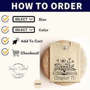 May include: A beige t-shirt with a black and white illustration of a book with flowers growing out of it. The text "Chapter 70" is printed below the book. The t-shirt is on a woven basket.