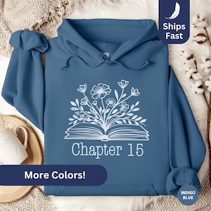May include: A blue hoodie with a white design of an open book with flowers growing out of it. The text "Chapter 15" is below the book. The hoodie has a hood and a kangaroo pocket.
