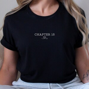 May include: Black t-shirt with the text "CHAPTER 15" in white, centered on the chest. A small heart design is below the text. The shirt has short sleeves and a crew neck.