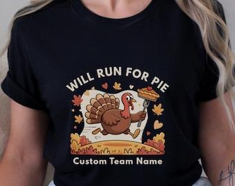 May include: Black t-shirt with a cartoon turkey running with a slice of pie. The text "WILL RUN FOR PIE" is above the turkey, and "Custom Team Name" is below. The design includes fall leaves and a heart.