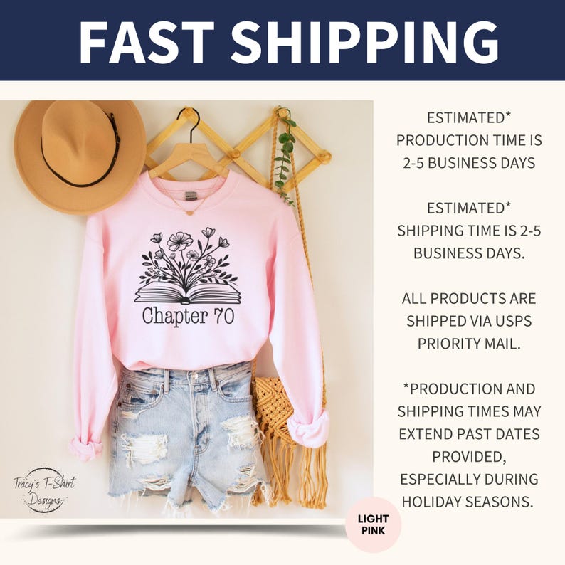 May include: A light pink sweatshirt with a black graphic of an open book with flowers growing out of it. The text "Chapter 70" is printed below the book. The sweatshirt is hanging on a wooden rack with a brown hat and a woven bag.