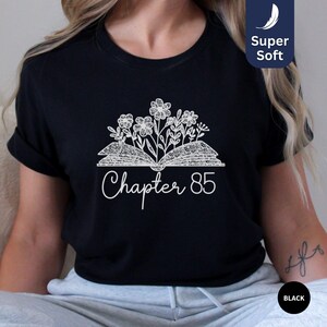 May include: Black t-shirt with a white design of an open book with flowers and the text "Chapter 85".