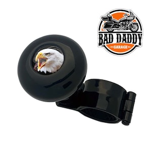 May include: Black steering wheel knob with a bald eagle image. The knob has a black metal clamp for attaching to a steering wheel. The text "BAD DADDY GARAGE" is on a sticker in the background.