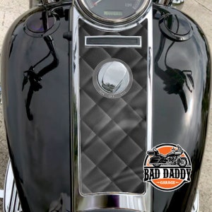 May include: Black motorcycle gas tank with a black and gray diamond patterned gas tank cover. The cover has a chrome trim and a chrome gas cap. The motorcycle has a Bad Daddy Garage logo sticker on the tank.