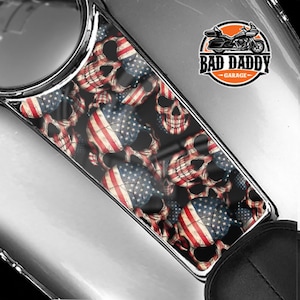 May include: A gas tank decal featuring a skull and crossbones design with an American flag pattern. The decal is black with red, white, and blue accents. The text "Bad Daddy Garage" is printed on the decal.