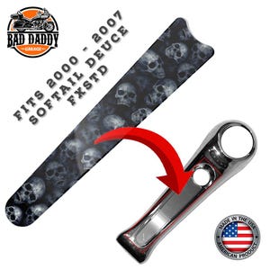May include: Motorcycle part with a skull pattern and chrome accent. The part is black with a repeating skull design and a shiny chrome piece. The text reads "FITS 2000 - 2007 SOFTAIL DEUCE FXSTD" and "MADE IN THE USA".