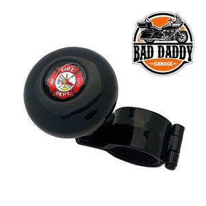 May include: Black steering wheel knob with a red and white fire department logo. The knob is attached to a black clamp.