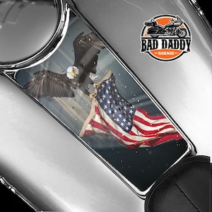 May include: A gas tank decal featuring a bald eagle with outstretched wings holding an American flag. The decal has a blue, white, and red color scheme and the text "Bad Daddy Garage".