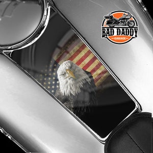 May include: A black and white gas tank decal featuring a bald eagle with a distressed American flag background. The decal has the text "Bad Daddy Garage" in a white circle with a red outline.
