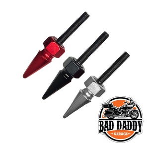 May include: Three metal motorcycle valve stem caps in red, black, and silver with a pointed tip. The caps are threaded and have a hexagonal nut. The image also includes a logo for "Bad Daddy Garage".