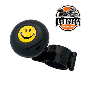 May include: Black steering wheel knob with a yellow smiley face design. The knob is attached to a black metal clamp. The text "BAD DADDY GARAGE" is visible in the background.