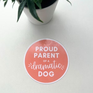 May include: A round, peach-colored sticker with white text that reads "Proud Parent of a dramatic dog".