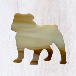 May include: A stained glass bulldog figurine in shades of tan and brown. The dog is standing, with its features and form clearly defined. The glass has a marbled effect, adding depth and visual interest to the piece. The background is a light wood grain.