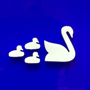May include: White swan and duck shapes on a blue background. The image features a large swan and three smaller duck shapes. The shapes are cut out and appear to be made of a solid white material.