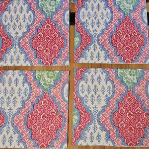 Op de afbeelding: Een set van vier vierkante onderzetters met een herhalend patroon van in elkaar grijpende vierpasvormen. Het ontwerp bevat tinten roze, lichtblauw en groen met ingewikkelde bloem- en plantmotieven die op elk oppervlak zijn gedrukt.