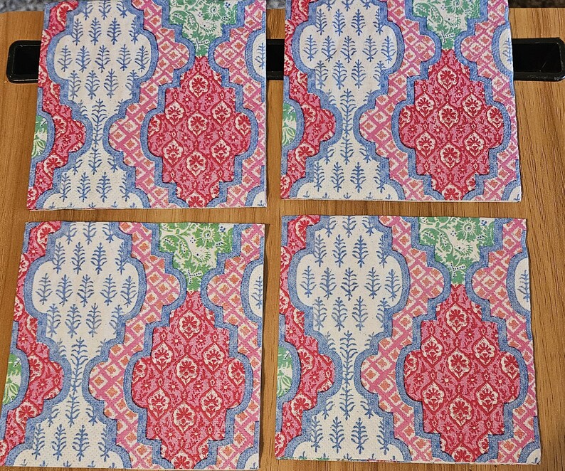 Op de afbeelding: Een set van vier vierkante onderzetters met een herhalend patroon van in elkaar grijpende vierpasvormen. Het ontwerp bevat tinten roze, lichtblauw en groen met ingewikkelde bloem- en plantmotieven die op elk oppervlak zijn gedrukt.